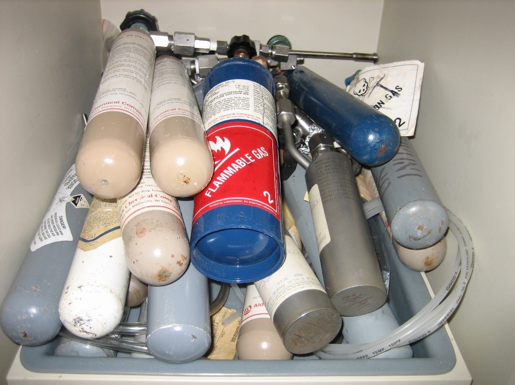 Lecture bottles on their sides inside of a chemical storage cabinet